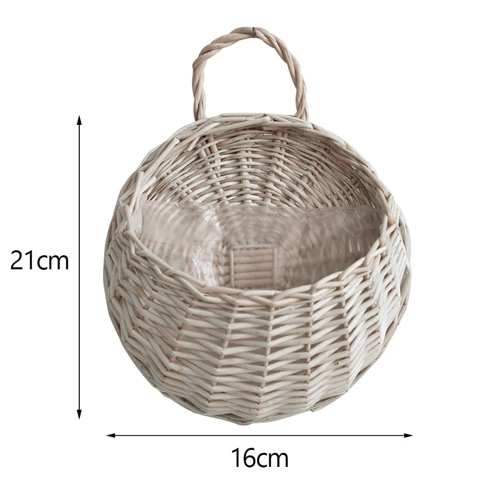The Hanging Planter is a handmade wicker rattan wall-mounted flower basket, 21 cm tall and 16 cm wide, shown from above. It features a handle, light natural color, visible weaving patterns, and adds charm to balcony, garden & home décor.