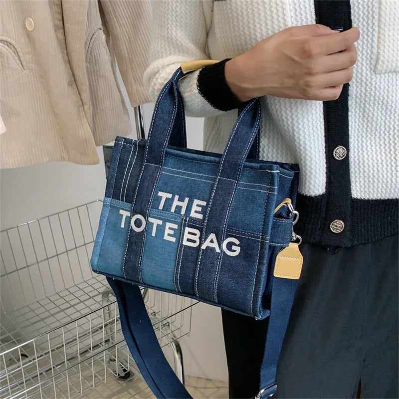 Person holding a blue tote bag with 'THE TOTE BAG' text, standing in a kitchen.