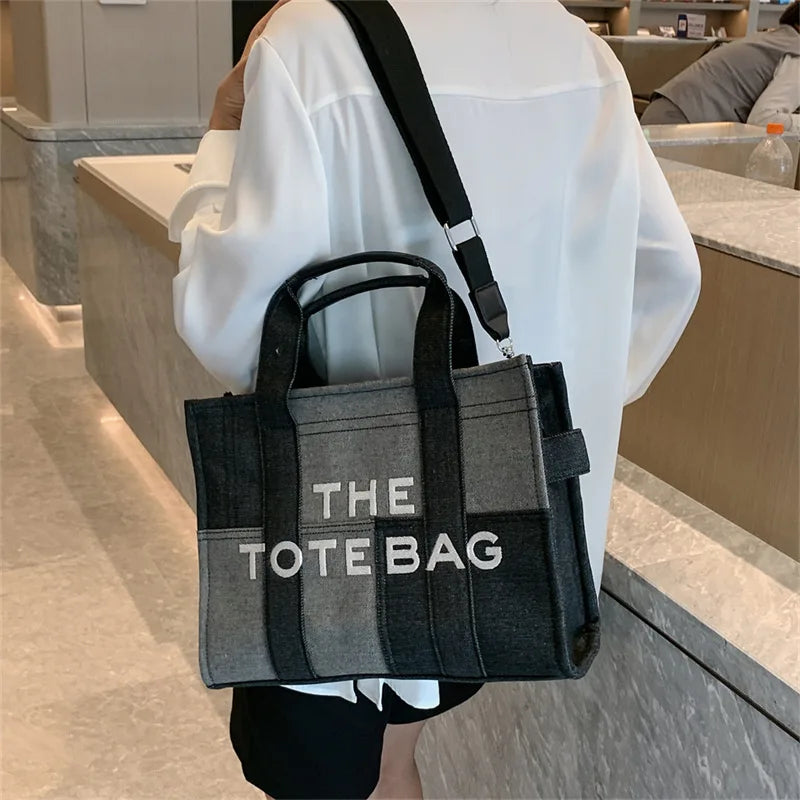Person holding a black tote bag with 'THE TOTE BAG' text in a bathroom setting