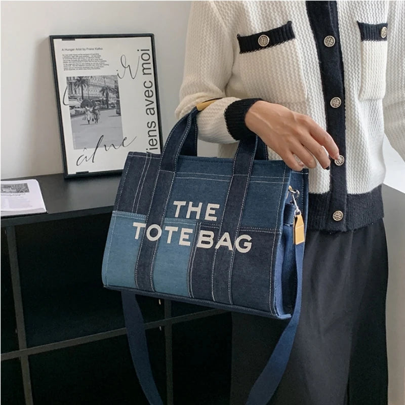 Person holding a blue tote bag with 'THE TOTE BAG' text in an indoor setting.