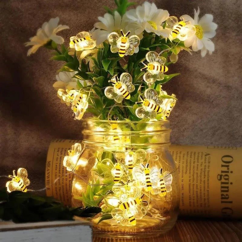 Jar with LED string lights shaped like bees and flowers on a wooden surface.