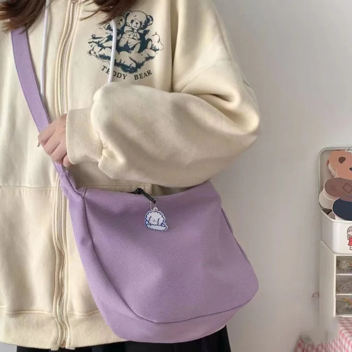 Person holding a purple bag with a teddy bear design, wearing a beige jacket with a teddy bear logo.