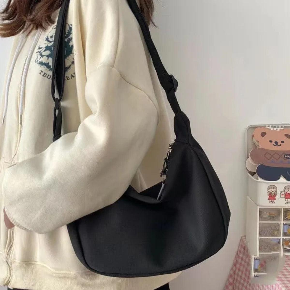 Person holding a black shoulder bag with a white wall and decorative items in the background