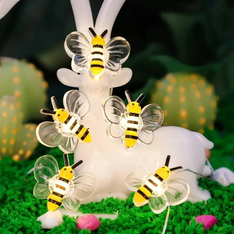 Decorative light set with bee-shaped lamps on a grassy surface with cacti in the background.