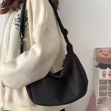 Person holding a black handbag against a white wall with a small decorative item.